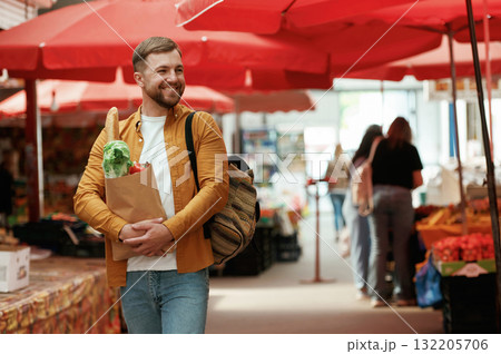 Cheerful, with products in paper bag. Handsome man is on the street market or bazaar Cheerful, with products in paper bag. Handsome man is on the street market or bazaar 132205706