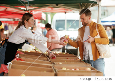 Giving apples. Man is buying products on the street market or bazaar from woman 132205830