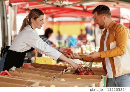 Taking apples. Man is buying products on the street market or bazaar from woman Taking apples. Man is buying products on the street market or bazaar from woman 132205834