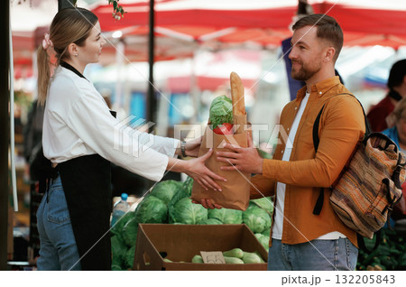 View from the side, vegetables. Man is buying products on the street market or bazaar from woman View from the side, vegetables. Man is buying products on the street market or bazaar from woman 132205843