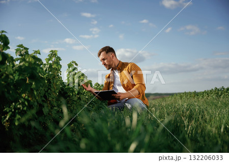 Quality control, with notepad. Handsome man is on the agricultural field at daytime Quality control, with notepad. Handsome man is on the agricultural field at daytime 132206033