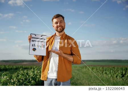 Graphs and business analytics on document, notepad. Handsome man is on the agricultural field at daytime 132206043
