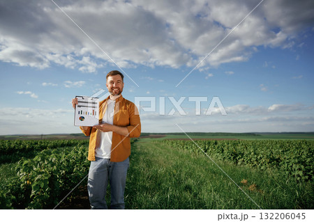 Graphs and business analytics on document, notepad. Handsome man is on the agricultural field at daytime Graphs and business analytics on document, notepad. Handsome man is on the agricultural field at daytime 132206045
