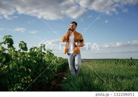 Talking by phone, holding notepad. Handsome man is on the agricultural field at daytime Talking by phone, holding notepad. Handsome man is on the agricultural field at daytime 132206051