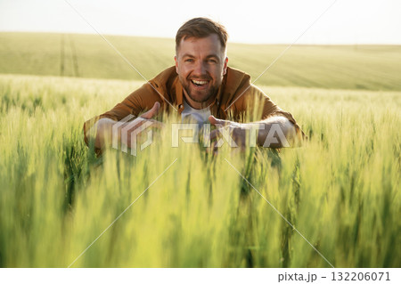 Embracing the growing wheat, smiling. Handsome man is on the agricultural field at daytime 132206071