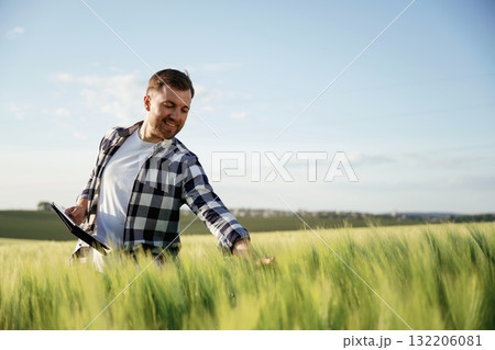 Black digital tablet in hands. Handsome man is on the agricultural field at daytime Black digital tablet in hands. Handsome man is on the agricultural field at daytime 132206081