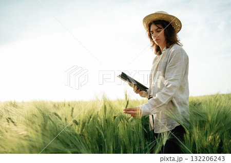 In straw hat, with tablet. Woman in white is on the agricultural wheat field In straw hat, with tablet. Woman in white is on the agricultural wheat field 132206243
