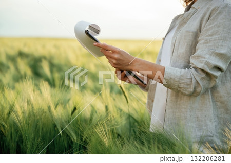 Notepad with documents in hands. Woman in white is on the agricultural wheat field 132206281