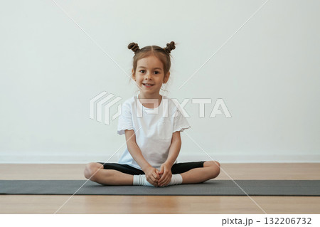 Cute little girl is sitting on the yoga mat and doing exercises Cute little girl is sitting on the yoga mat and doing exercises 132206732