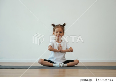 Cute little girl is sitting on the yoga mat and doing exercises Cute little girl is sitting on the yoga mat and doing exercises 132206733