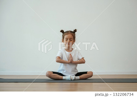 Cute little girl is sitting on the yoga mat and doing exercises 132206734