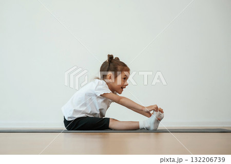Side view, stretching. Cute little girl is sitting on the yoga mat and doing exercises Side view, stretching. Cute little girl is sitting on the yoga mat and doing exercises 132206739