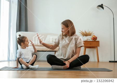 Smiling, positive facial expression. Young woman with little girl are doing yoga at home 132206842