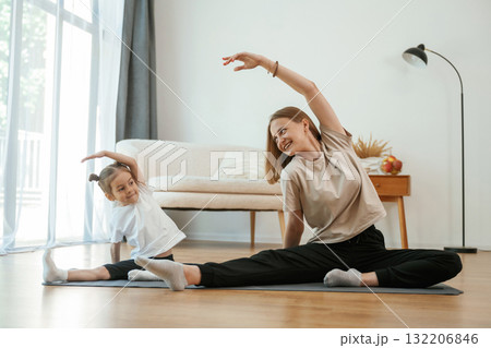 To the side, stretching. Young woman with little girl are doing yoga at home To the side, stretching. Young woman with little girl are doing yoga at home 132206846