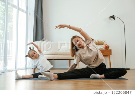 To the side, stretching. Young woman with little girl are doing yoga at home 132206847