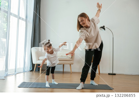 Focused on the exercise. Young woman with little girl are doing yoga at home Focused on the exercise. Young woman with little girl are doing yoga at home 132206855