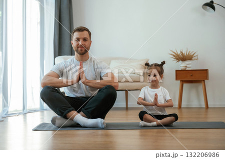 Lotus pose. Father with little daughter are doing yoga at home 132206986