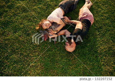 Top view, lying on the grass. Man and woman are with dog on the field Top view, lying on the grass. Man and woman are with dog on the field 132207152