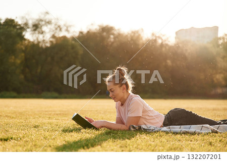 Woman is lying down on the summer field and reading a book Woman is lying down on the summer field and reading a book 132207201