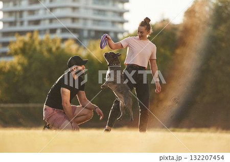 Playing with a rubber toy. Man and woman are with dog on the field Playing with a rubber toy. Man and woman are with dog on the field 132207454