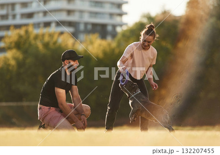 Active time spending, with rubber toy. Man and woman are with dog on the field 132207455