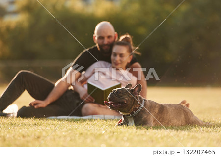 Weekend time, resting and sitting. Man and woman are with dog on the field Weekend time, resting and sitting. Man and woman are with dog on the field 132207465
