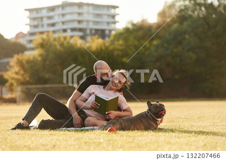 Weekend time, resting and sitting. Man and woman are with dog on the field Weekend time, resting and sitting. Man and woman are with dog on the field 132207466