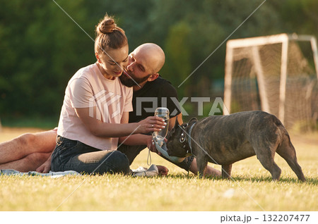 Giving the water. Man and woman are with dog on the field 132207477