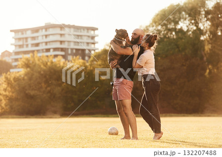 Side view, standing and holding animal. Man and woman are with dog on the field 132207488