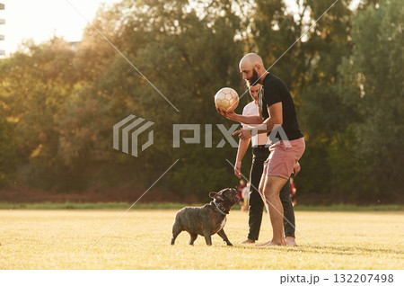 Using soccer ball, playing. Man and woman are with dog on the field 132207498