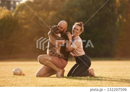 Positive facial expression, resting. Man and woman are with dog on the field 132207506