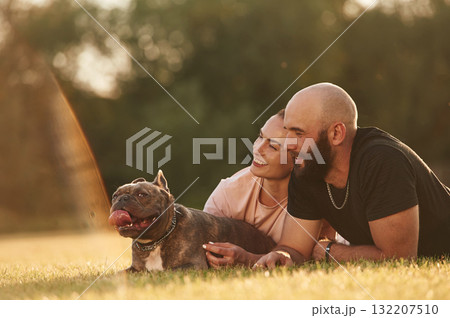 Calm, lying down on the ground. Man and woman are with dog on the field Calm, lying down on the ground. Man and woman are with dog on the field 132207510