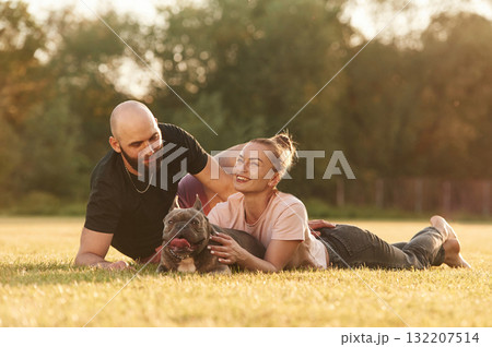 Positive facial expression, resting. Man and woman are with dog on the field 132207514
