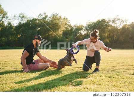 Active time spending, with rubber toy. Man and woman are with dog on the field 132207518