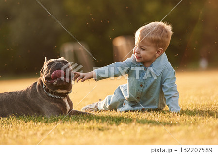 Sitting on the ground. Cute little boy is with dog on the field Sitting on the ground. Cute little boy is with dog on the field 132207589