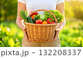 Woman holds a basket of fresh vegetables in a sunlit garden during daytime 132208337