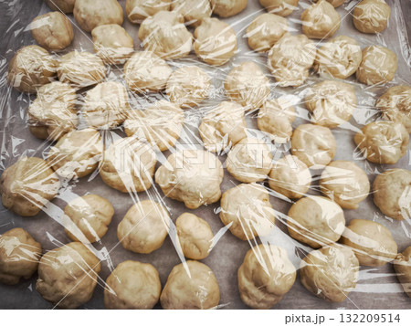 Dough balls resting and rising under plastic wrap on baking sheet Dough balls resting and rising under plastic wrap on baking sheet 132209514