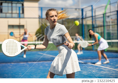 Young woman playing paddle tennis against team of women 132210425