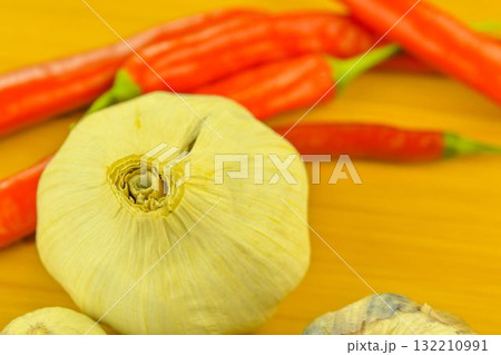 Garlic cloves and red chili peppers on a wooden cutting board. The concept of cooking and vegetables in the home. Garlic - Allium sativum is a species of bulbous flowering plants in the genus Allium Garlic cloves and red chili peppers on a wooden cutting board. The concept of cooking and vegetables in the home. Garlic - Allium sativum is a species of bulbous flowering plants in the genus Allium 132210991