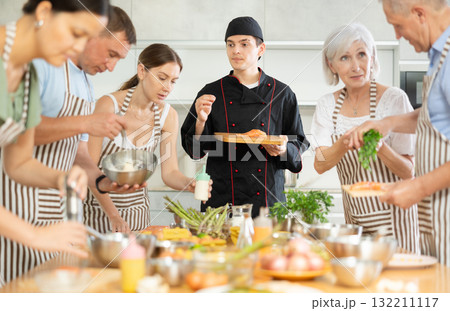 Chef in uniform teaches cooking class students how to clean and cut salmon fillet 132211117