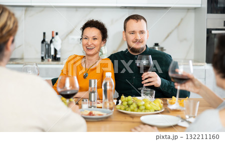 Two married couples are sitting at table, enjoying food and wine, chatting, talking, laughing. Two married couples are sitting at table, enjoying food and wine, chatting, talking, laughing. 132211160
