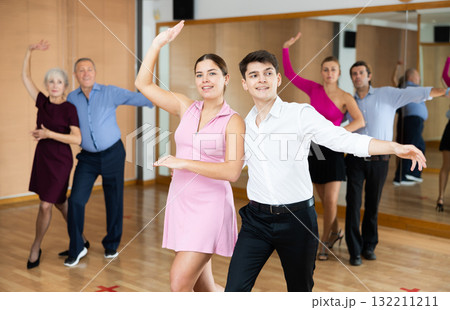 Cheerful young guy and girl practicing ballroom dances in ballroom Cheerful young guy and girl practicing ballroom dances in ballroom 132211211