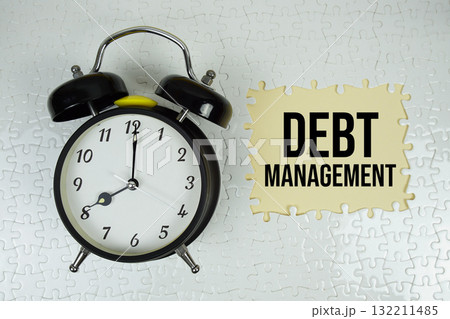 Jigsaw puzzle with a missing piece with "Debt Management" and alarm clock on yellow background Jigsaw puzzle with a missing piece with "Debt Management" and alarm clock on yellow background 132211485