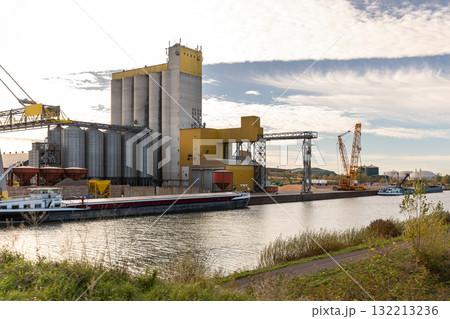 Large industrial facility silos cranes stands Mittellandkanal cargo ships docked loading operations. Calm water industrial equipment reflect economic activity and regional infrastructure development 132213236