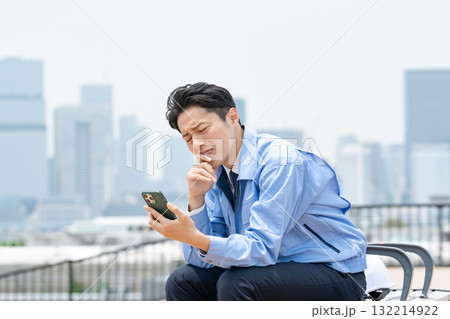 スマホを見て悩む作業服の男性　 132214922