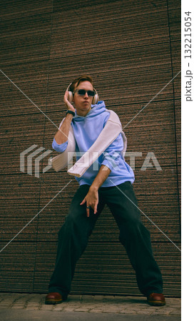 Man dancing in blue hoodie and headphones near textured brown wall Man dancing in blue hoodie and headphones near textured brown wall 132215054