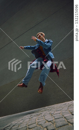 Man jumping in denim jacket and boots between tall stone walls 132215096