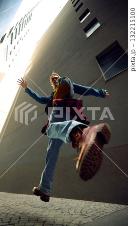 Man jumping in city alley wearing denim jacket and red checkered shirt Man jumping in city alley wearing denim jacket and red checkered shirt 132215100