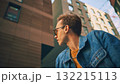 Man in denim jacket with yellow sweater looking sideways among high city buildings 132215113