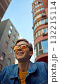 Smiling man in denim jacket with yellow shirt looking up between buildings 132215114